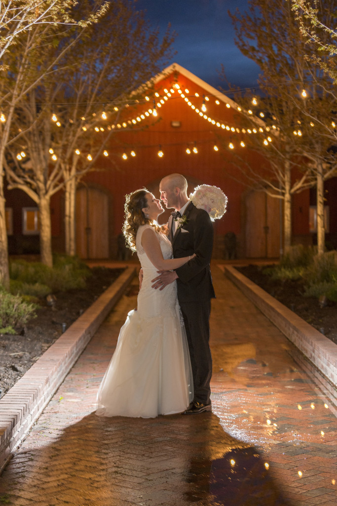 Beautiful night shot of bride and groom at Crooked Willow Farm with Off Camera Flash, there are beautiful lights in the background, bride and groom are standing and embracing looking at each other and almost kissing
