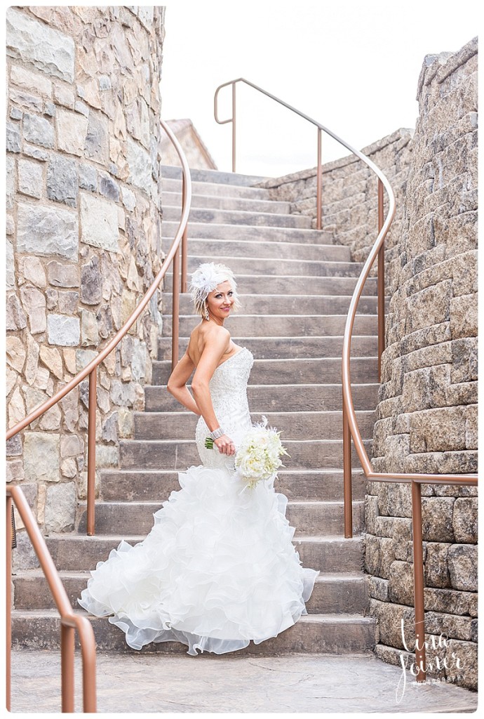 Bride stands at the bottom of a stone stair case displaying her wedding dress