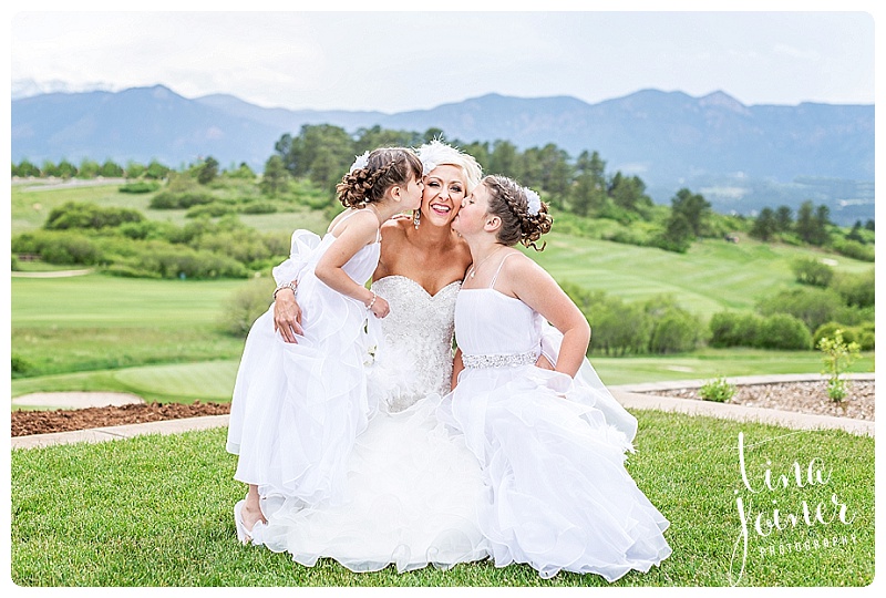 Flower girls kissing bride on the cheek with lovely mountain views
