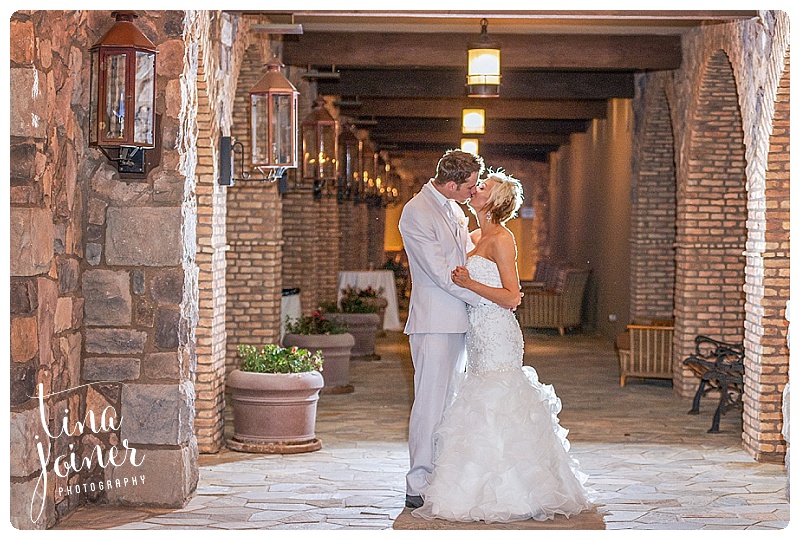 Bride and groom stand kissing and embracing with dramatic lighting behind them at night portrait