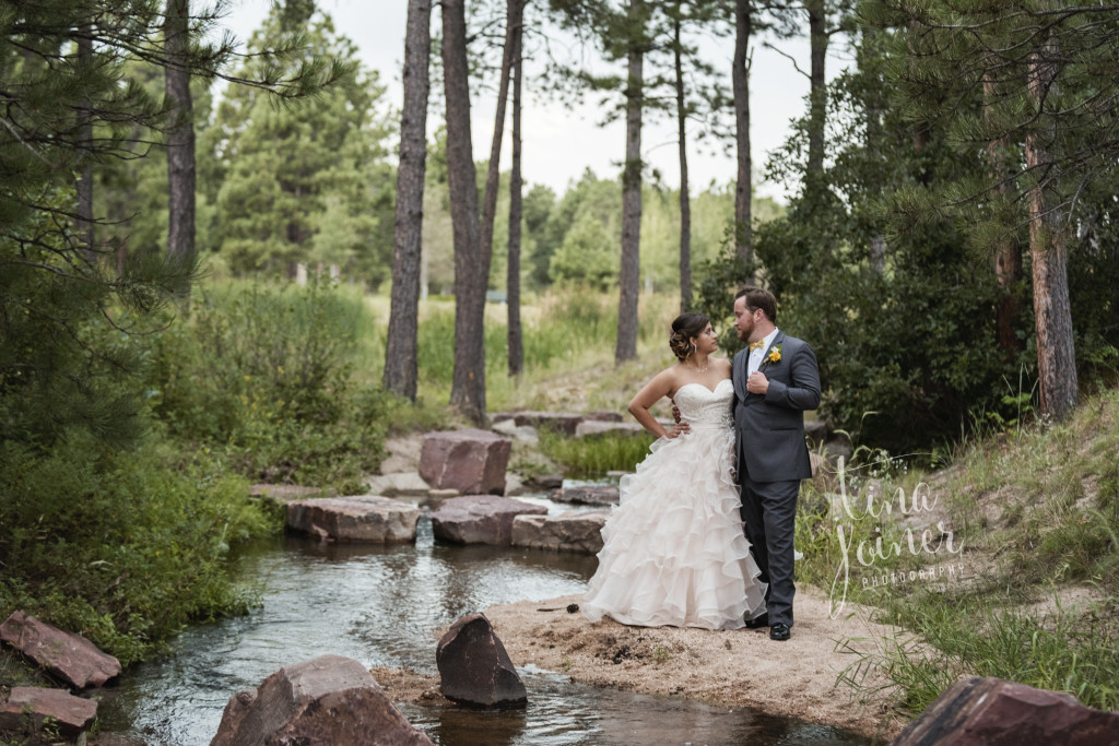 bride and groom stand next to a creek looking at each other and arms around each other