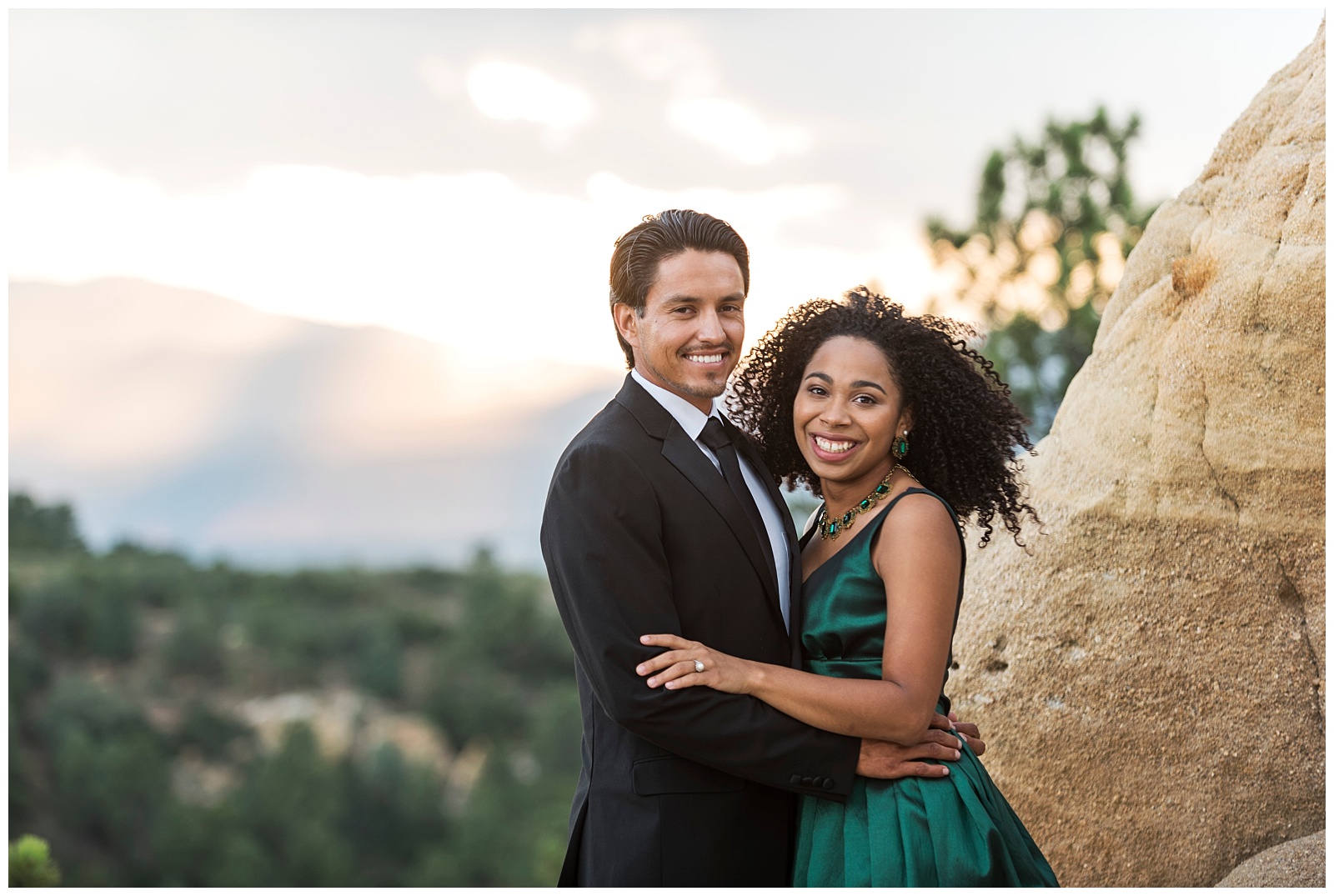 Couple standing and embracing with lovely mountain views behind them, they are smiling and looking at the camera