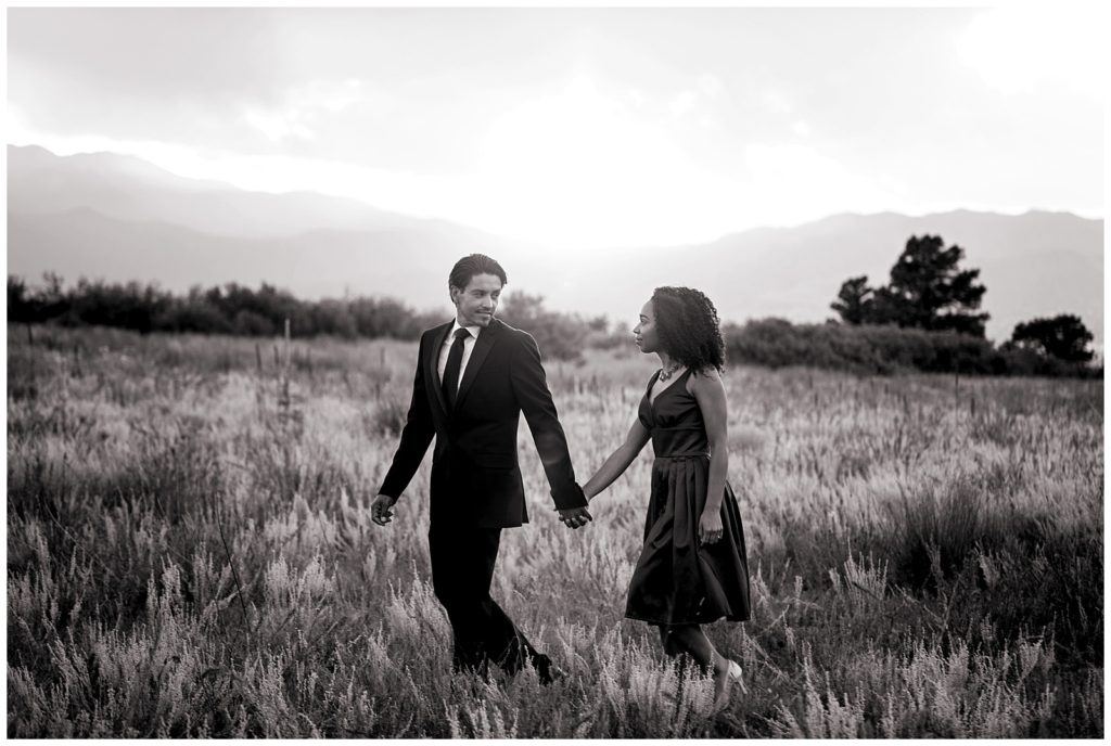 Samuel and Pam walk holding hands through a field at Palmer Park with majestic mountain views at sunset