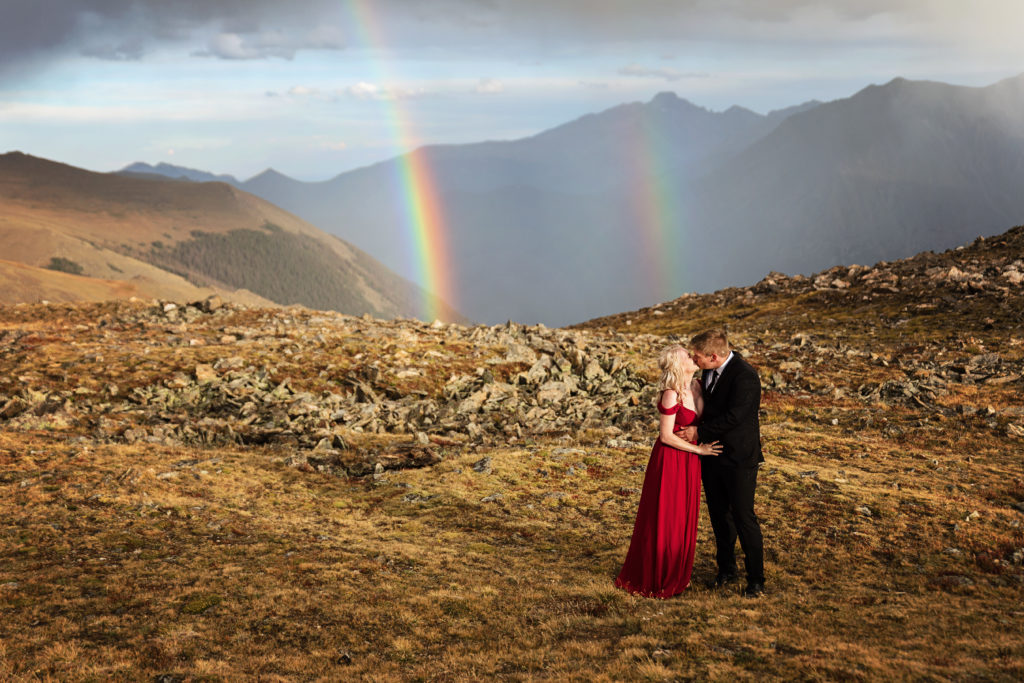 Mollie and Kurtis are kissing in Rocky Mountain National Park with a double rainbow behind them
