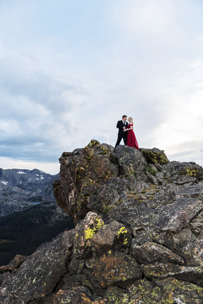 Mollie and Kurtis stand at the top of a mountain embracing as the wind whips through their hair, 