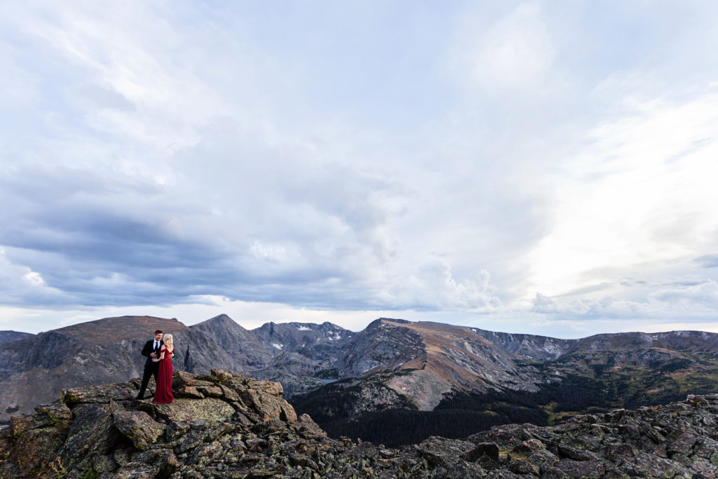 Kurtis and Mollie stand in Rocky Mountain National Park above the tree line with wide open views of the blue sky and mountain range