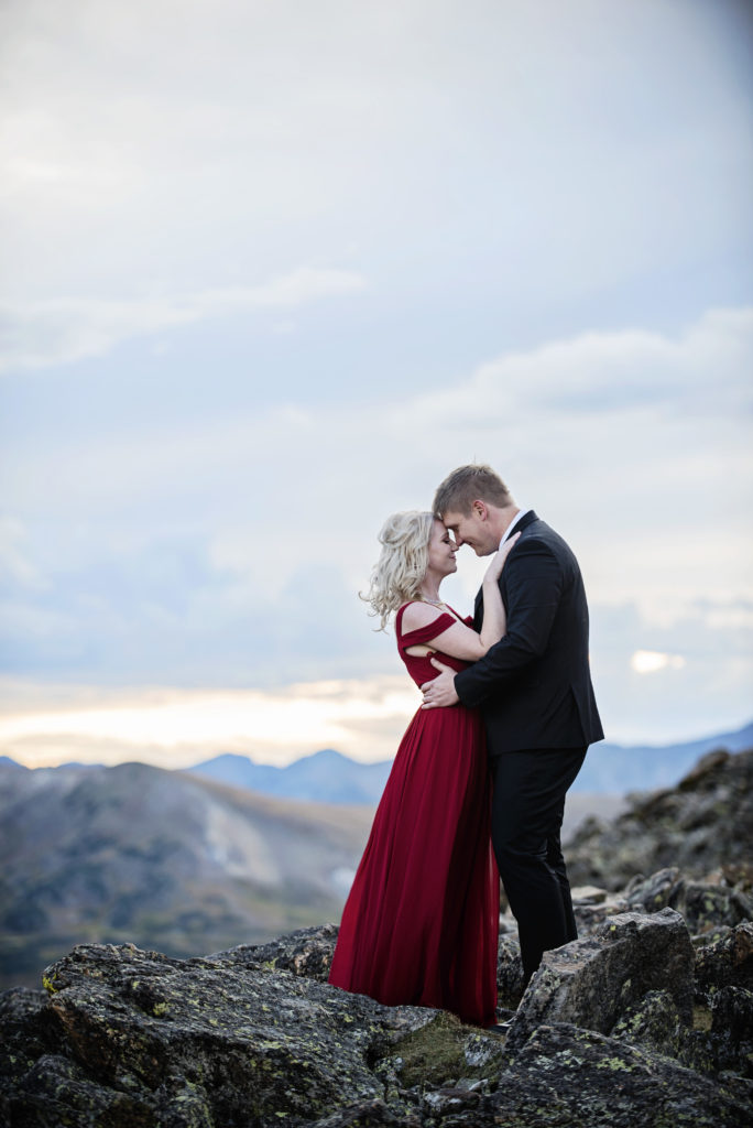 Curtis and Mollie stand on a mountain top with their foreheads together eyes closed and smiling, 
