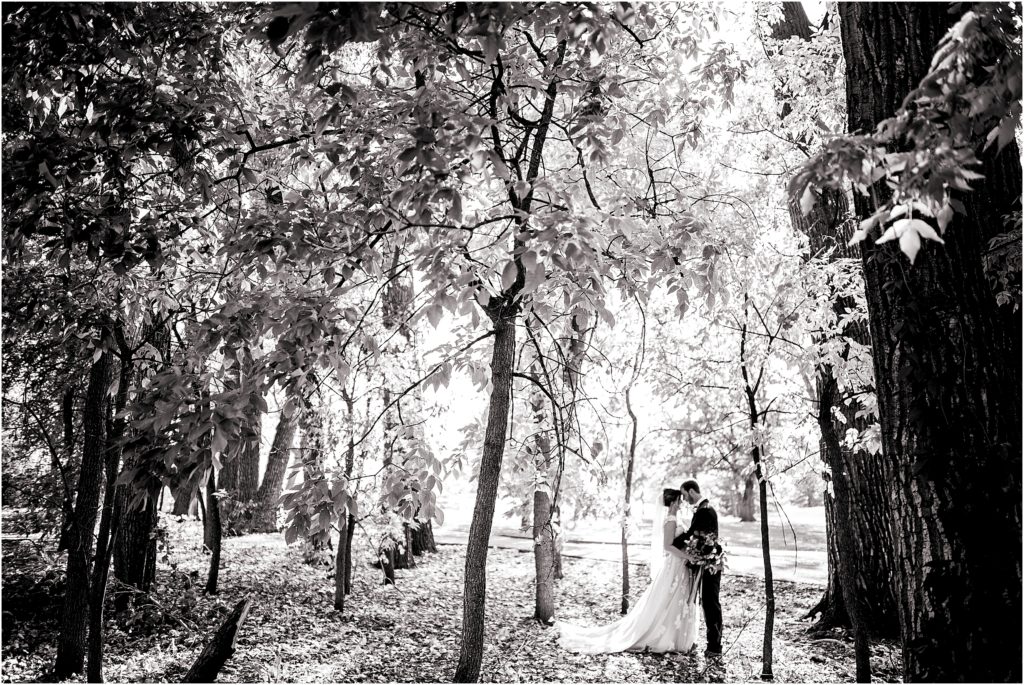 bride and groom stand in a forest surrounded by trees in black and white, bride and groom have their foreheads together and are facing each other