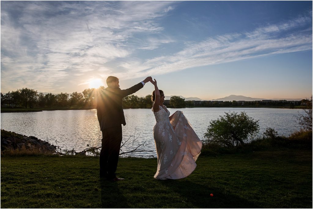 bride and groom dance in the sunset with a pond and mountains behind them