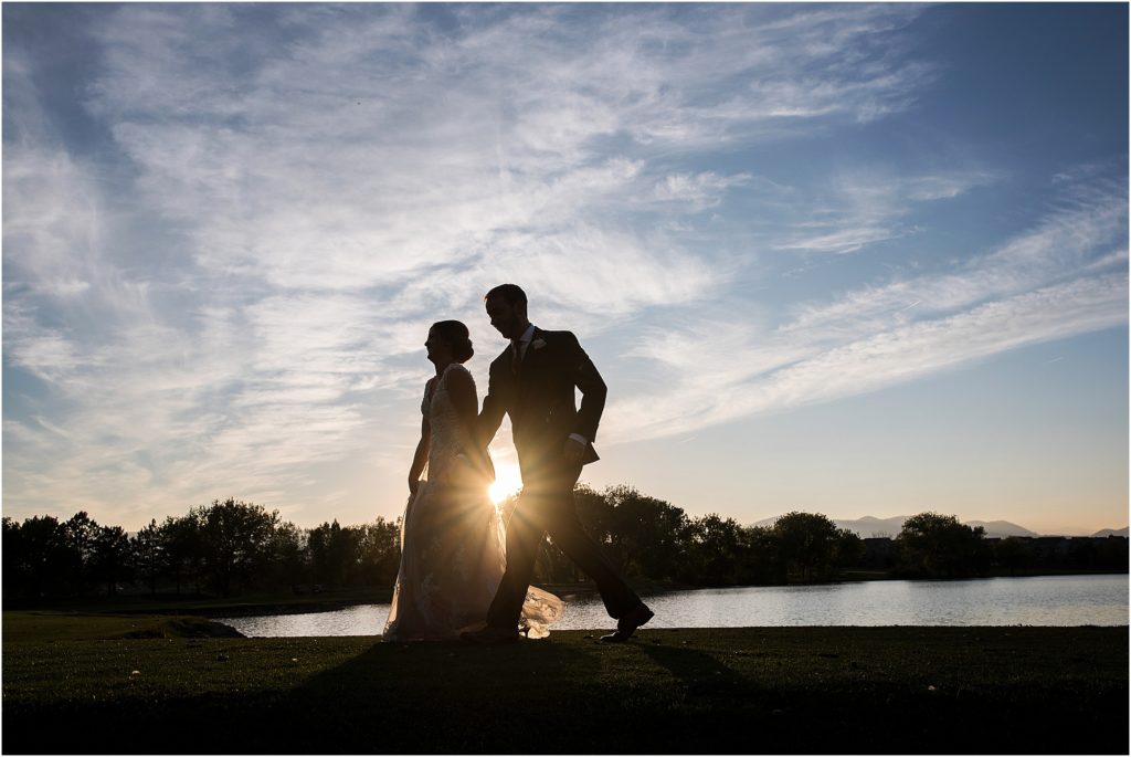 silhouette of bride and groom walking and smiling with a beautiful blue sky at sunset
