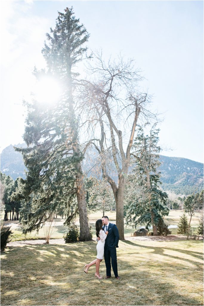 Scenic image of mountains and trees where a couple embrace and kiss wearing formal clothes at the broadmoor