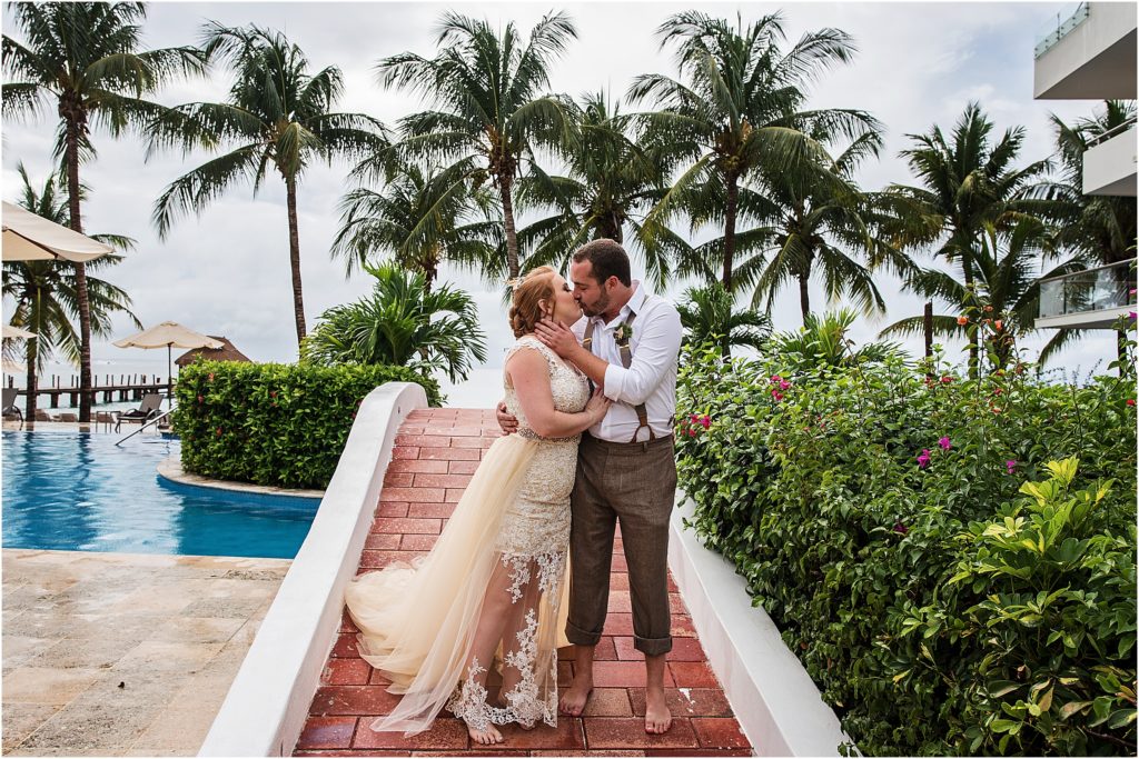 bride and groom stand barefoot on red brick path embracing and kissing at their destination wedding in Cozumel