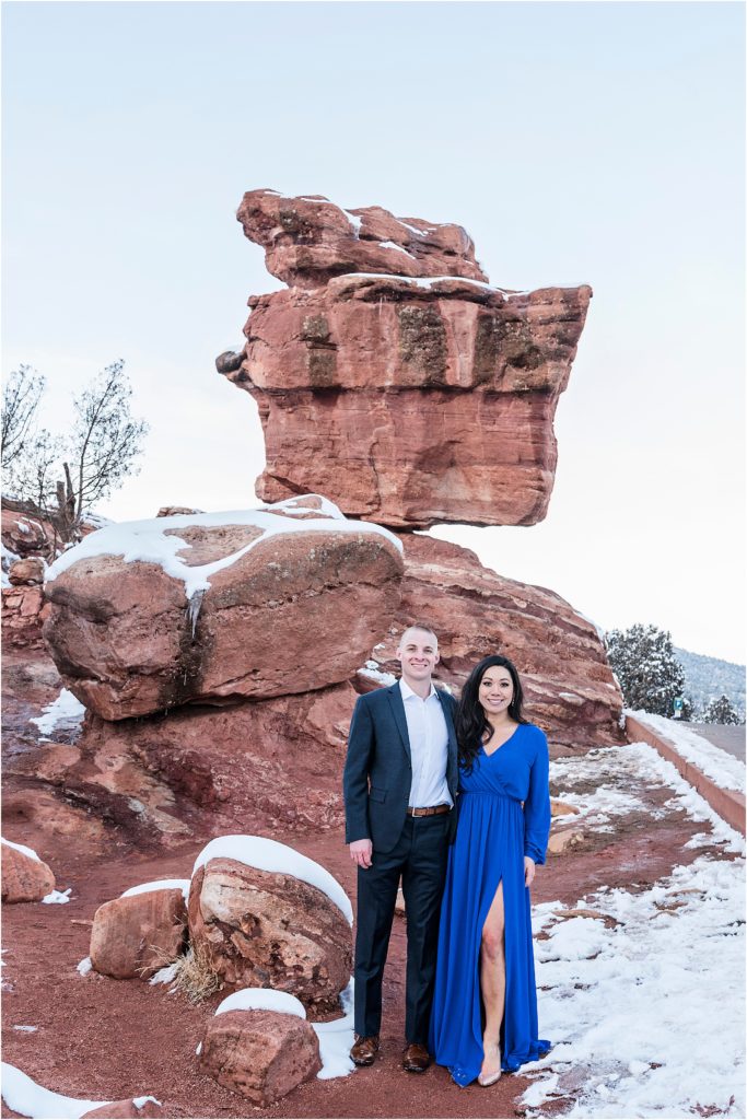 Couple stands in formal clothes in front of balance rock at Garden of the Gods in winter