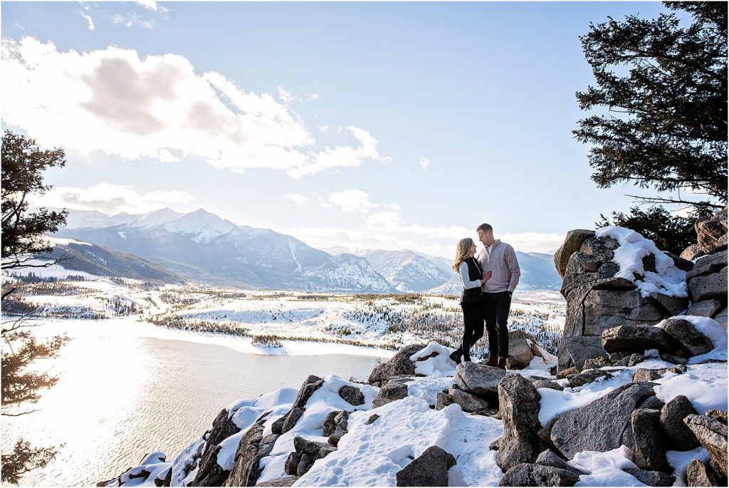Couple stand embracing and looking at each other at Sapphire Point, near Breckenridge, Colorado, with stunning mountain views behind them in winter