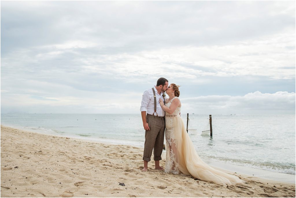 Bride and groom stand kissing on a beach
