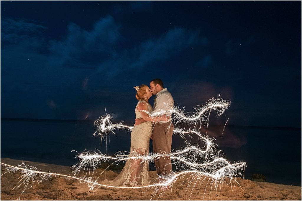 bride and groom stand embracing and kissing with a sparkler circling them at night