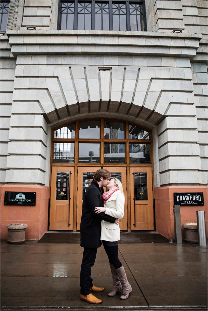 Engaged couple kiss romantically in front of downtown building doors