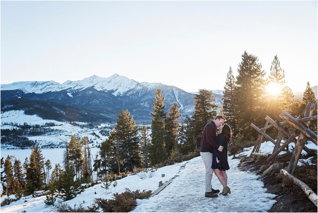 man and woman kissing on a trail near breckenridge in winter, forest and mountain views behind them