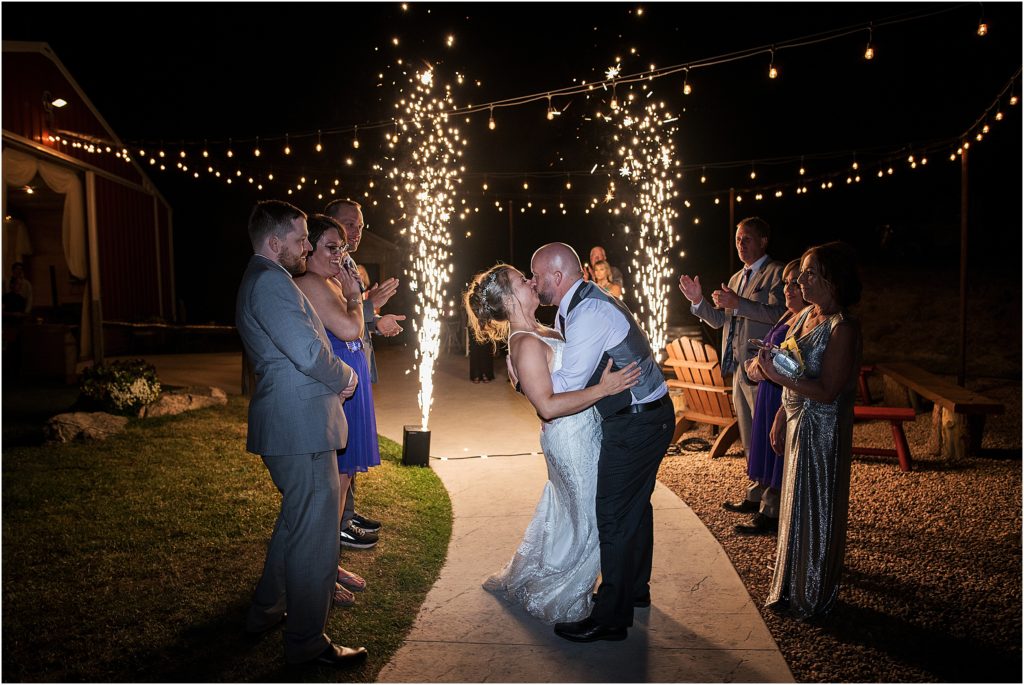 Dramatic wedding exit with pyrotechnics shooting sparkling fire into the sky behind bride and groom, groom is kissing and dipping bride
