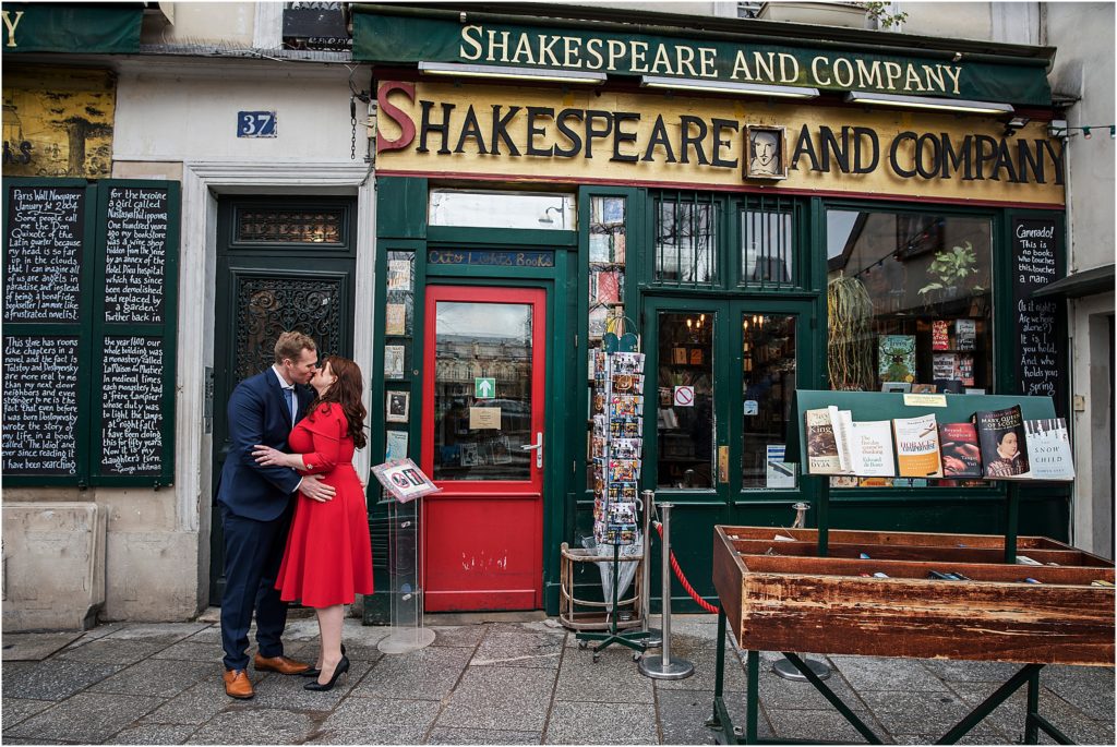 Engaged couple stand embracing and kissing in front of Shakespeare and Company in Paris