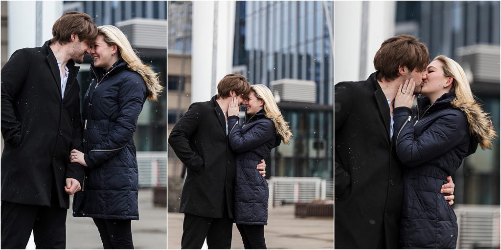 Mark and Rachel embrace and kiss while they are bundled up in winter coats and the snow falls in the city