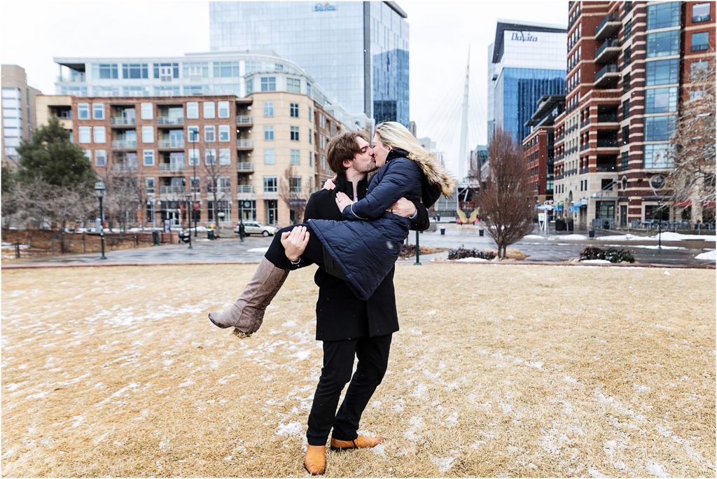 Mark is holding Rachel in his arms in a downtown Denver park while snow is falling
