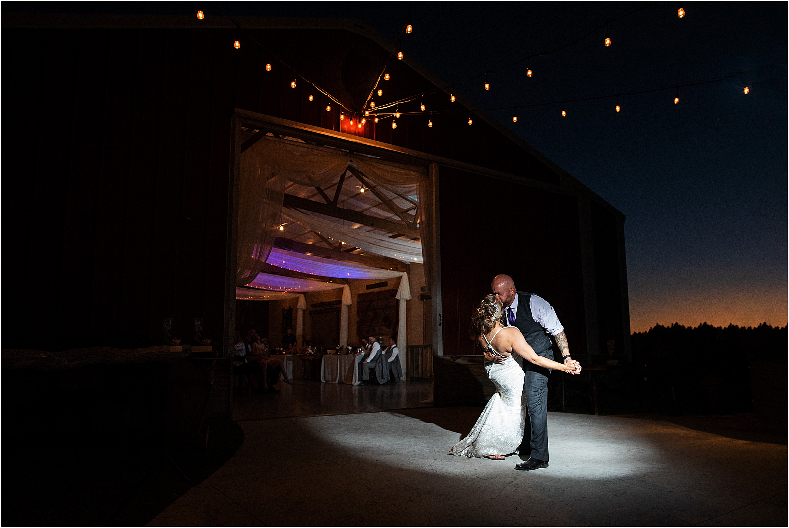 Dramatic image of bride and grooms first dance captured by Tina Joiner a Wedding Photographer in Colorado, groom dips bride as spotlight shines directly on them and everything else is dark, they are kissing