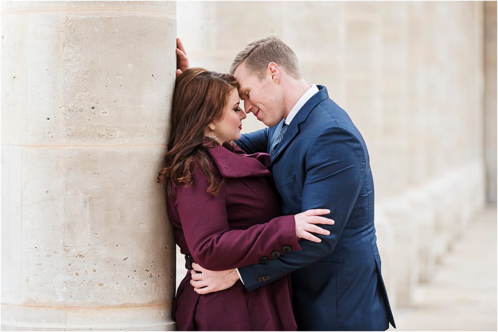 Meghan and Joost standing in a row of columns in paris, france, they are embracing romantically with their foreheads together and eyes closed about to kiss