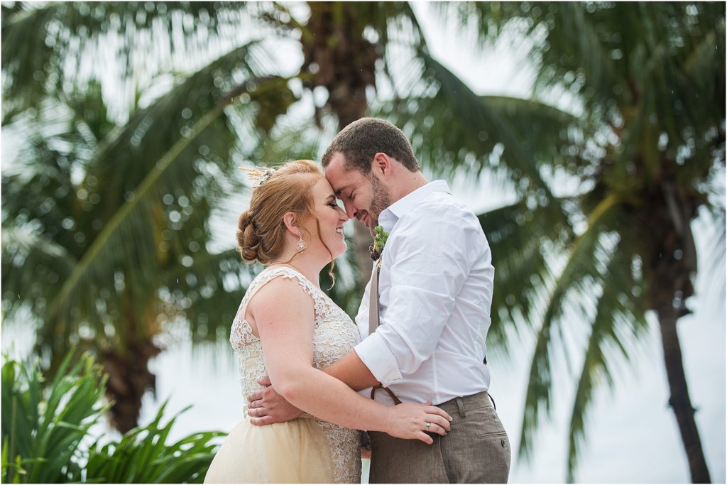 bride and groom embracing with their foreheads together smiling with their eyes closed with palm trees behind them