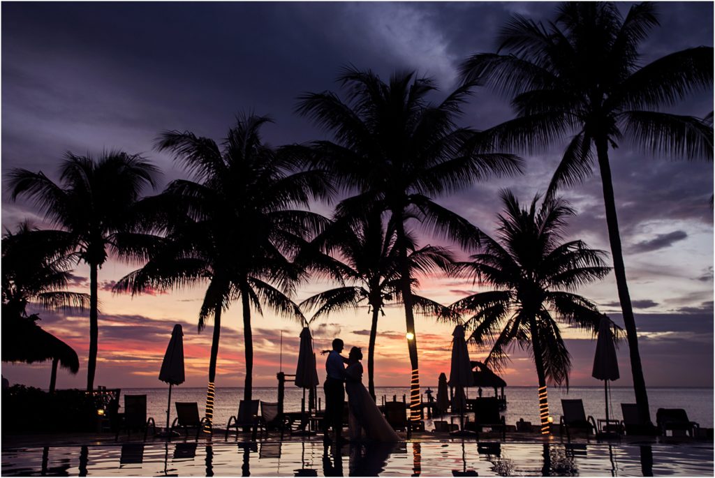 Stunning silhouette of bride and groom and tall palm trees at infinity pool at sunset