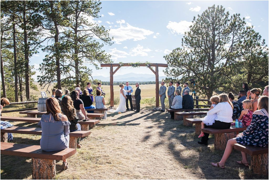 Bryan and Lori standing at their wedding ceremony in front of their family and friends with mountain views and blue skies behind them