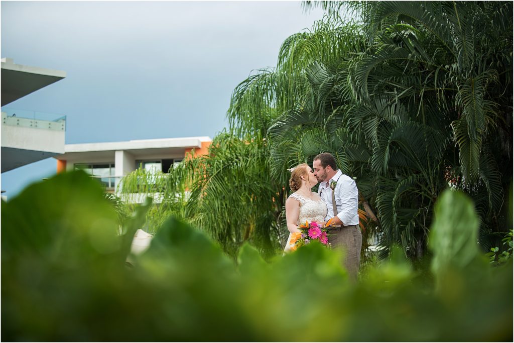 bride and groom kiss with tropical leaves in the background and foreground at this destination wedding
