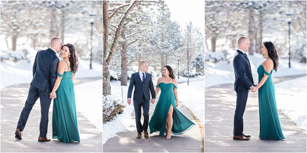 Engaged couple walk on a path at the Broadmoor in winter with snow and ice all around, they are wearing formal clothes, he is in a suit and tie and she is wearing a green floor length gown with a slit to her thigh