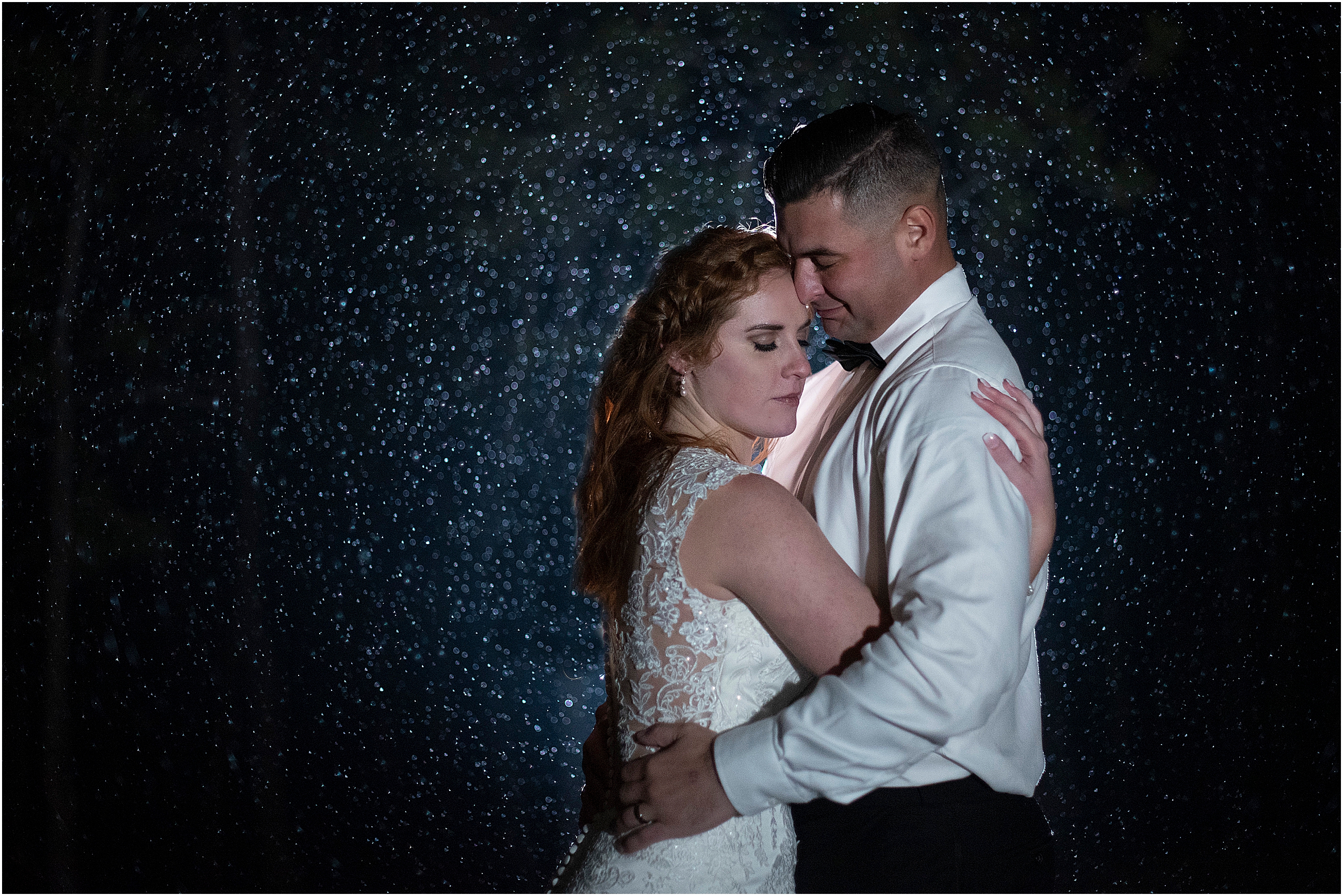Jeff and Cassidy stand and embrace while the snow falls all around them at night during their winter wedding in black forest, colorado