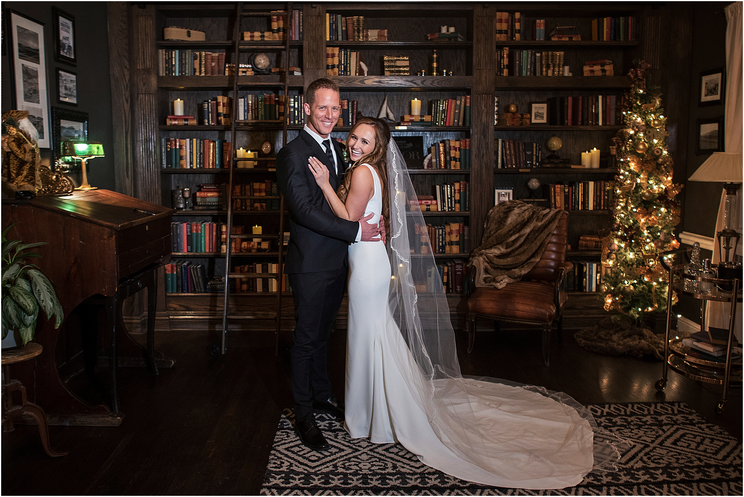 Bride and groom are standing and embracing and smiling and laughing after their wedding ceremony, they are standing in the library with a Christmas tree behind them at the Manor House