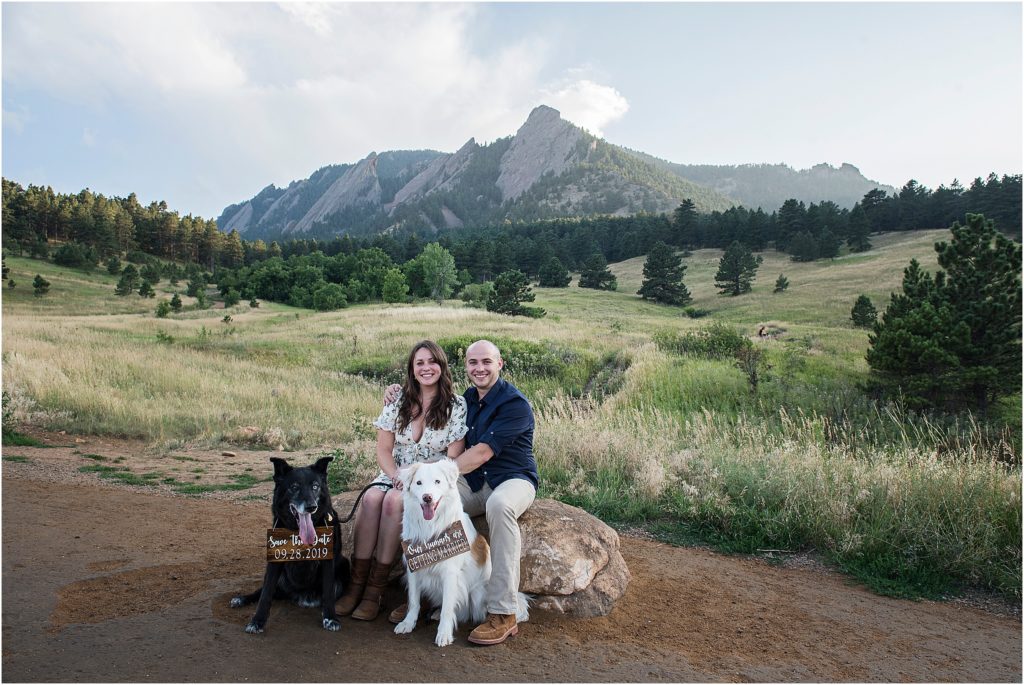 Couple with their dogs at Chautauqua Flatirons near boulder with their dogs wearing save the date signs