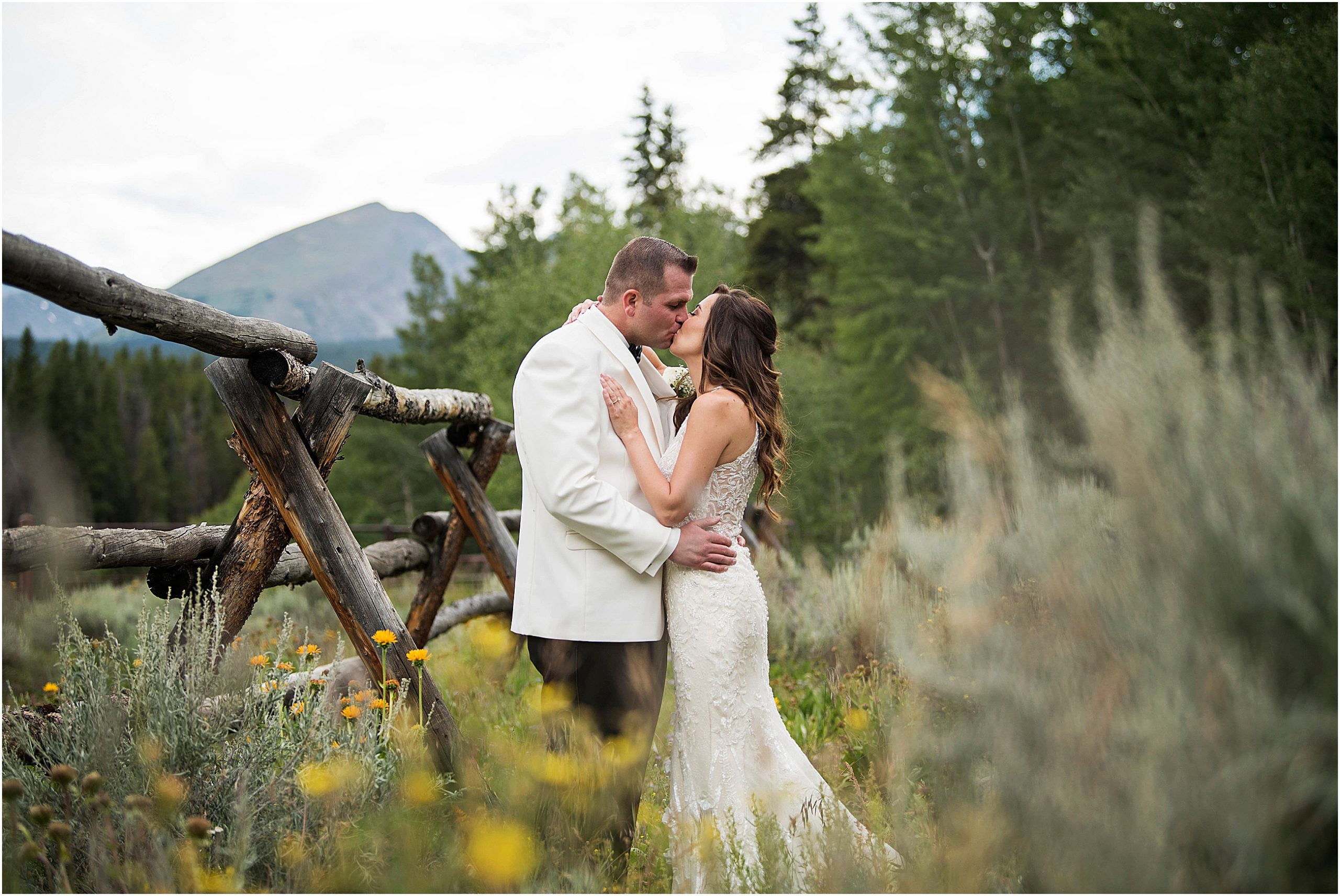 Bride and groom stand embracing and kissing with mountain views in Breckenridge surrounded by yellow wildflowers