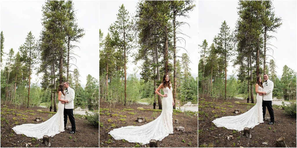 Bride and groom stand in a forested area embracing each other as groom kisses bride on the forehead.