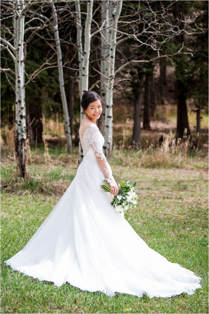 Emily in her wedding dress smiling on a fresh green lawn and aspen trees behind.