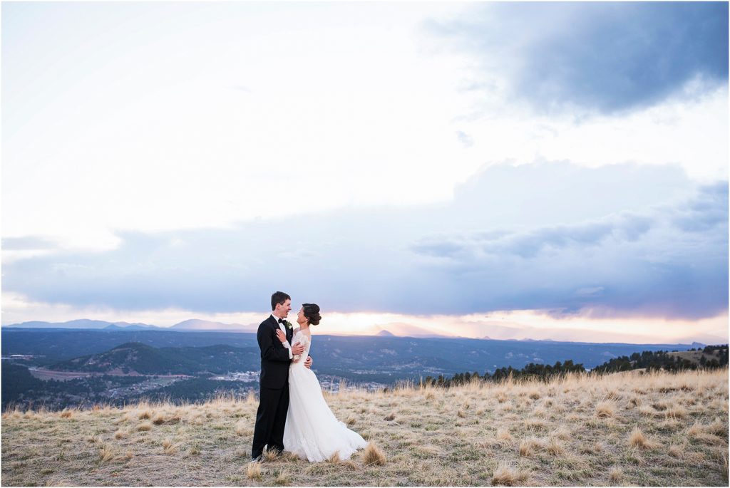 Bride and groom stand and embrace while talking in a location with distant mountain views.