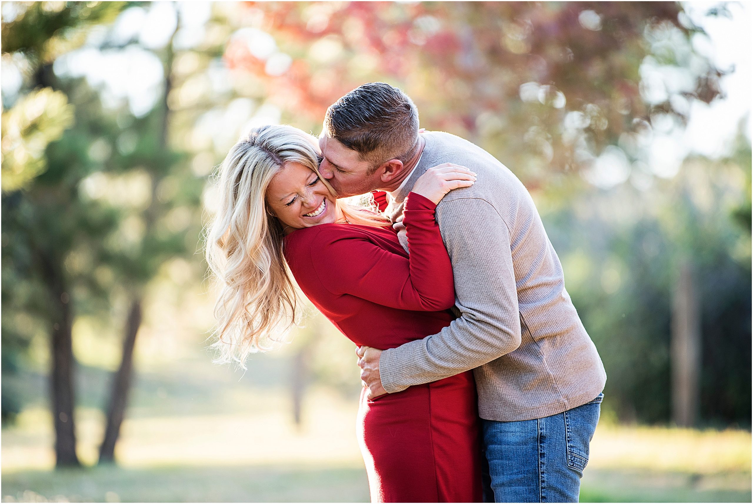 Jordan laughs while Brian holds her tight and kisses her cheek with red fall leaves behind them.