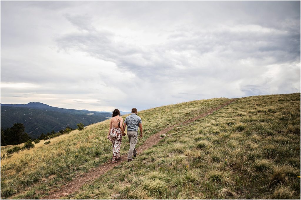 Engaged couple walk hand in hand up a hillside in Colorado