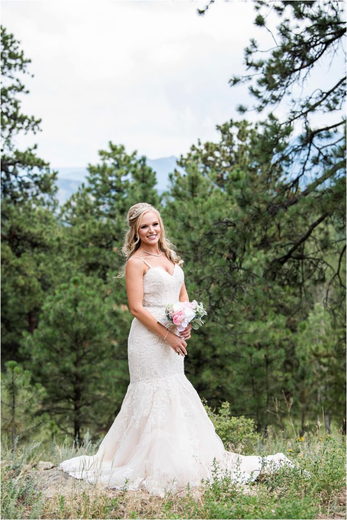 Breanda stands in her wedding dress with mountain views behind and evergreens.
