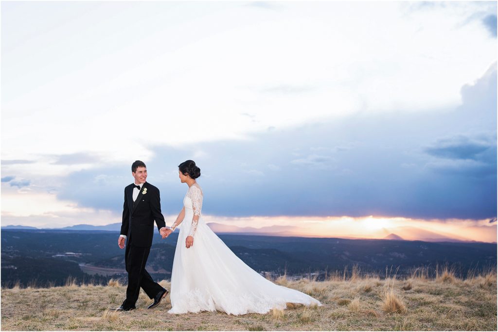 Bride and groom walk hand in hand on top of a mountain at sunset with amazing views in colorado.
