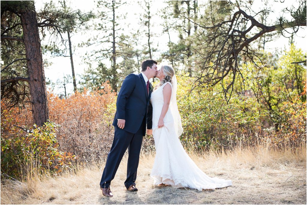 Bride and groom kiss with fall leaves behind them
