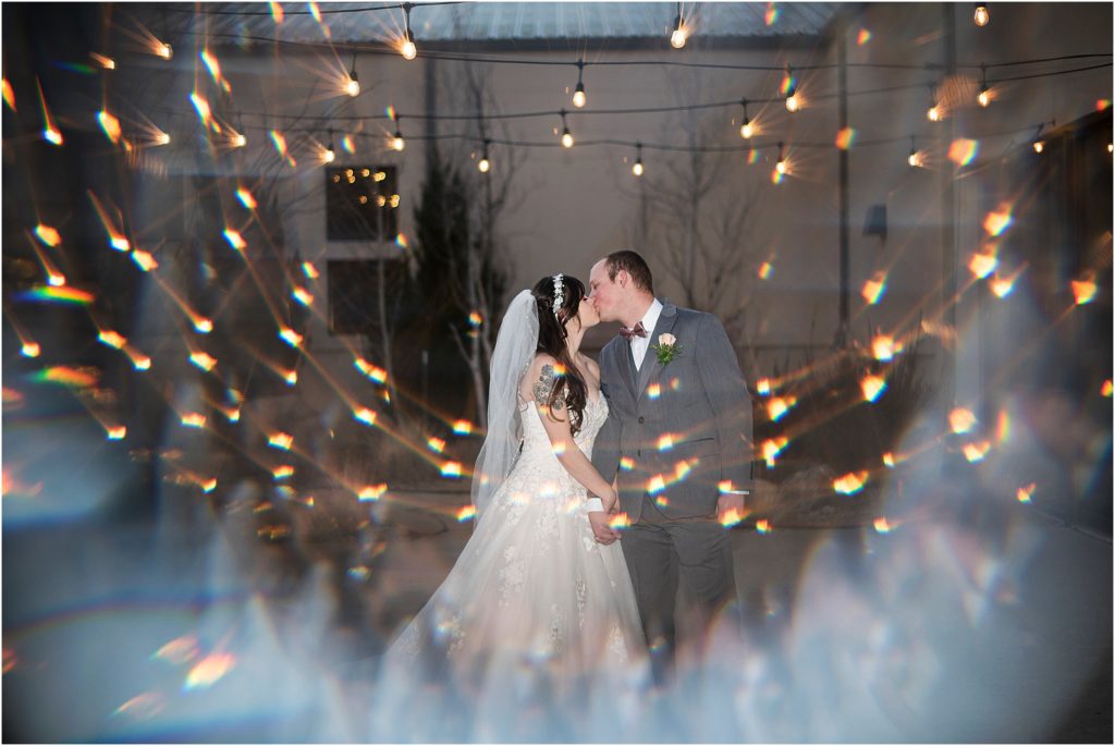 Bride and green surrounded by lights as they kiss in the evening.