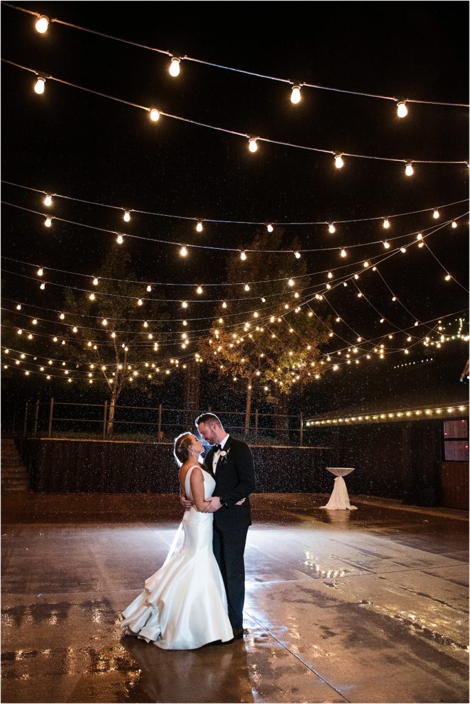 Josh and Lacy stand under the patio lights in the light rain at night after their wedding.