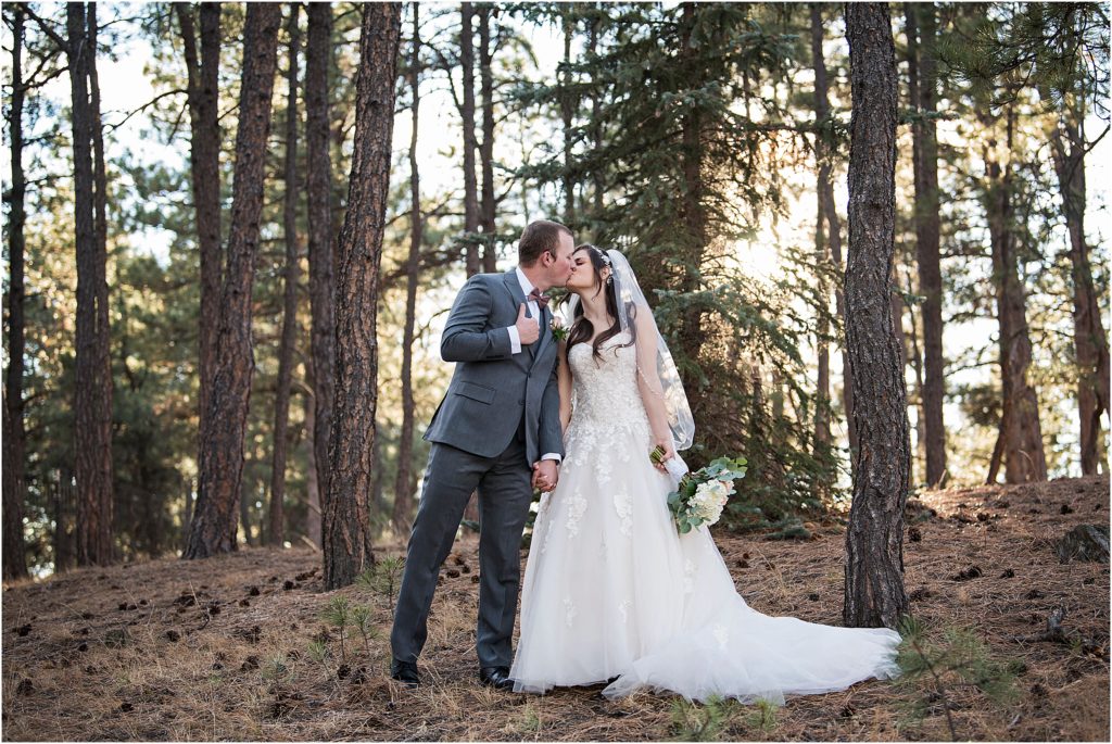 Ryan and Amanda stand in the forest holding hands and kissing on their wedding day.