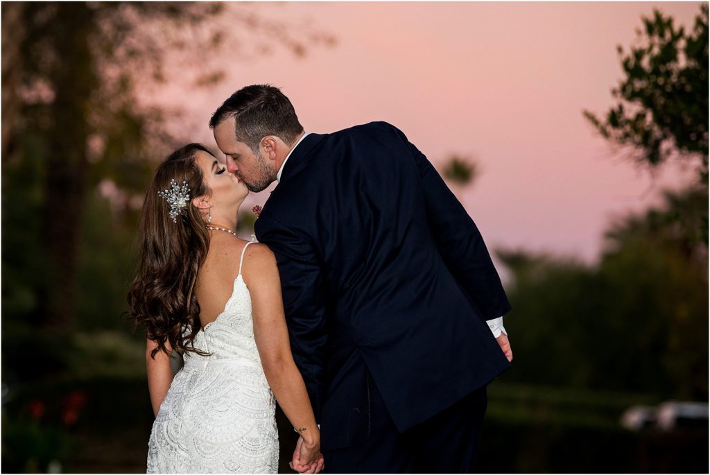 Bride and groom kiss with a pink sky behind them at sunset at their destination wedding.