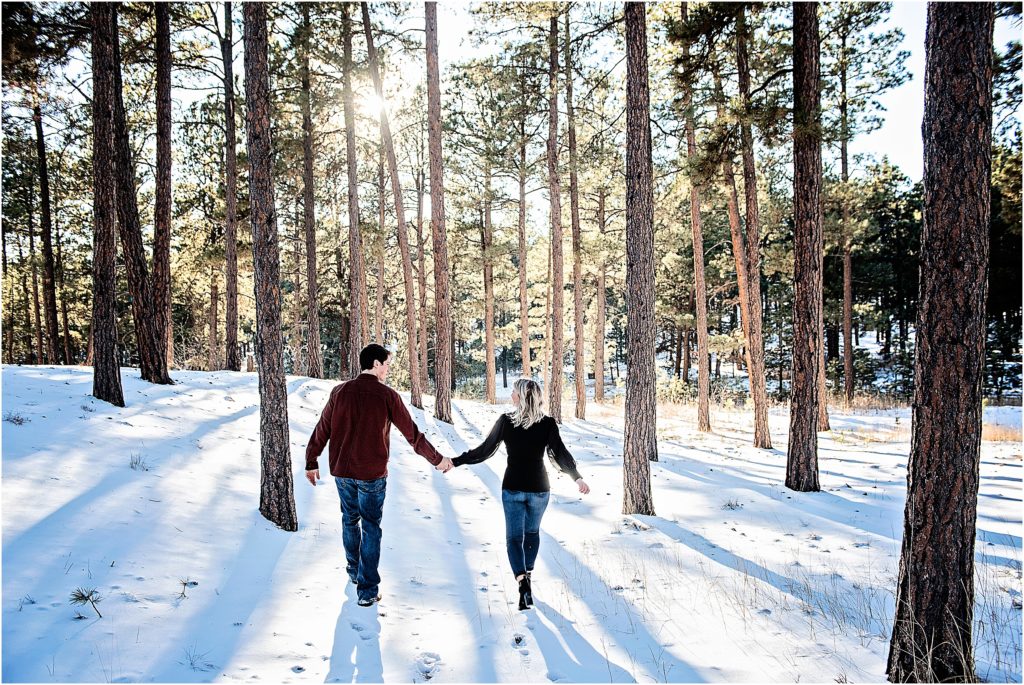 couple walks away looking at each other in a forest with snow all around